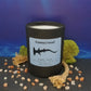 A black glass vessel with art of a hammerhead shark on a light blue label rests on a black slate, surrounded by moss and sea salt.